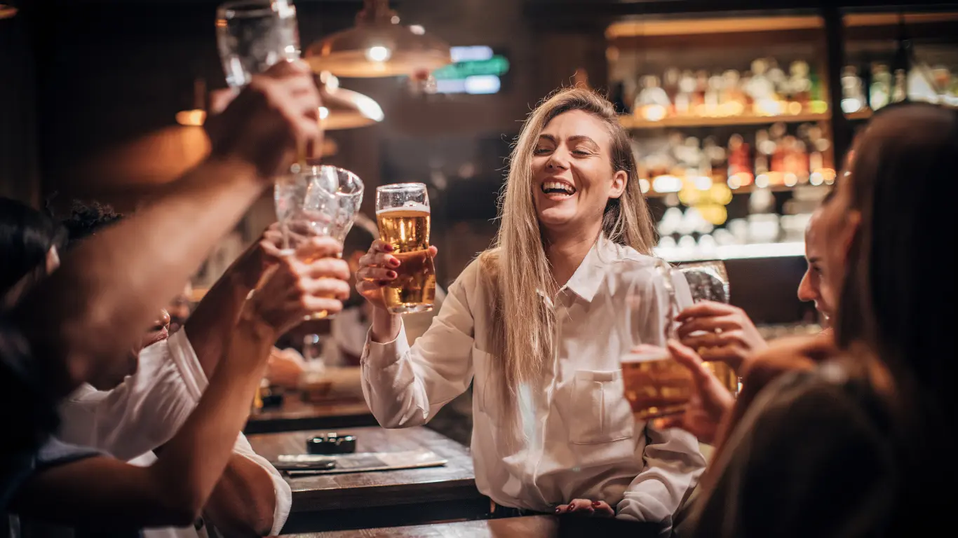 Ragazza al pub che si diverte e ride con amici con birra in mano